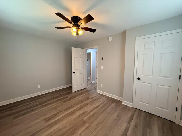 an empty room with wooden floor chandelier fan and windows