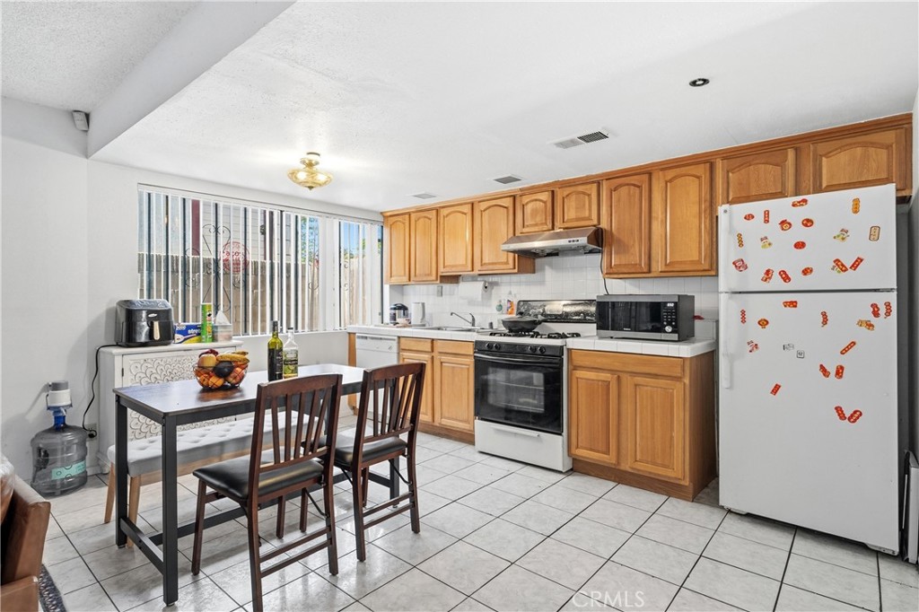 9471 Cortada Street El Monte, CA 91733 - Photo 7 of 27 a kitchen with stainless steel appliances granite countertop a stove a refrigerator a dining table and chairs with wooden floor