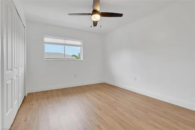 an empty room with wooden floor chandelier fan and windows