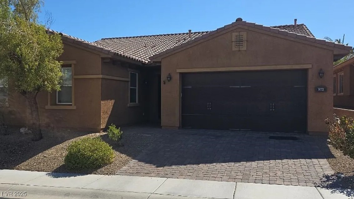 Ranch-style home featuring decorative driveway, a garage, and stucco siding