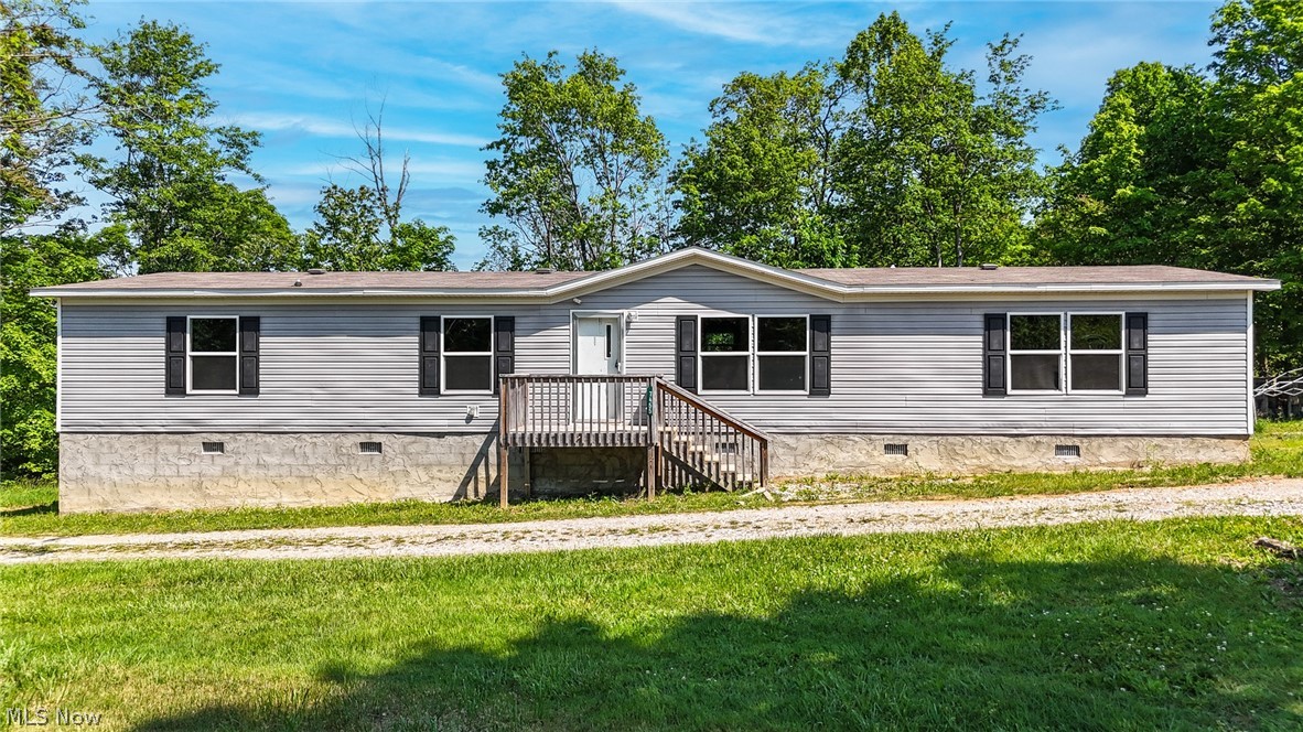 Single-story manufactured home featuring light gray siding, dark window shutters, and a central wooden entry deck
