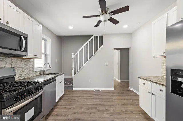 a kitchen with stainless steel appliances a sink a stove top oven a chimney cabinets and wooden floor