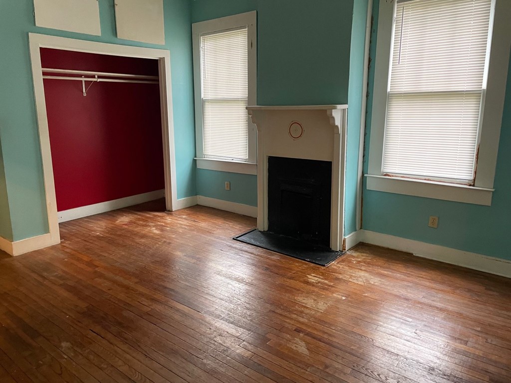 223 8th Street Columbus, GA 31901 - Photo 5 of 6 an empty room with wooden floor a fireplace and windows