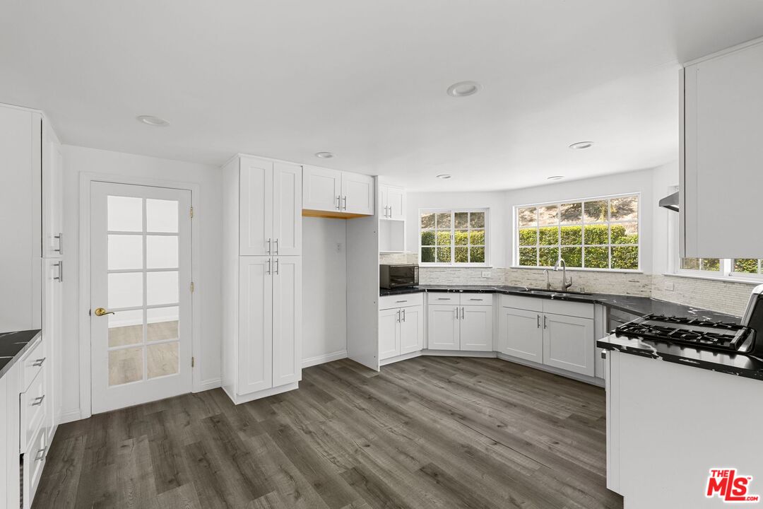 18657 Kirkcolm Lane Porter Ranch, CA 91326 - Photo 7 of 22 a kitchen with granite countertop a stove a sink and white cabinets with wooden floor next to windows