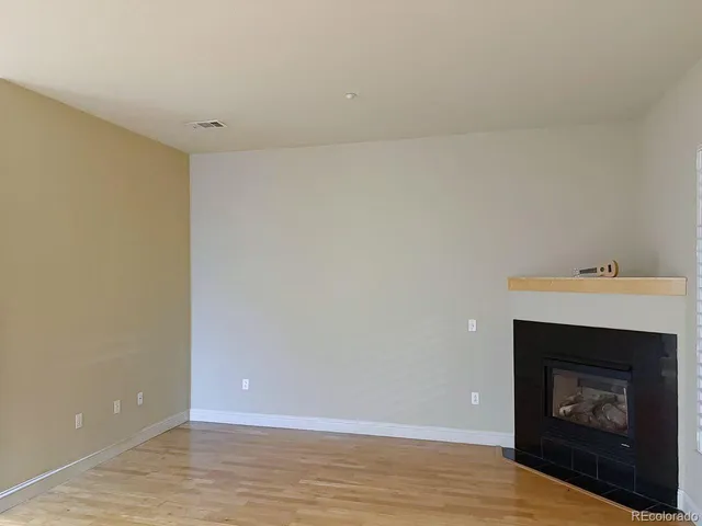 a view of an empty room with wooden floor and a fireplace