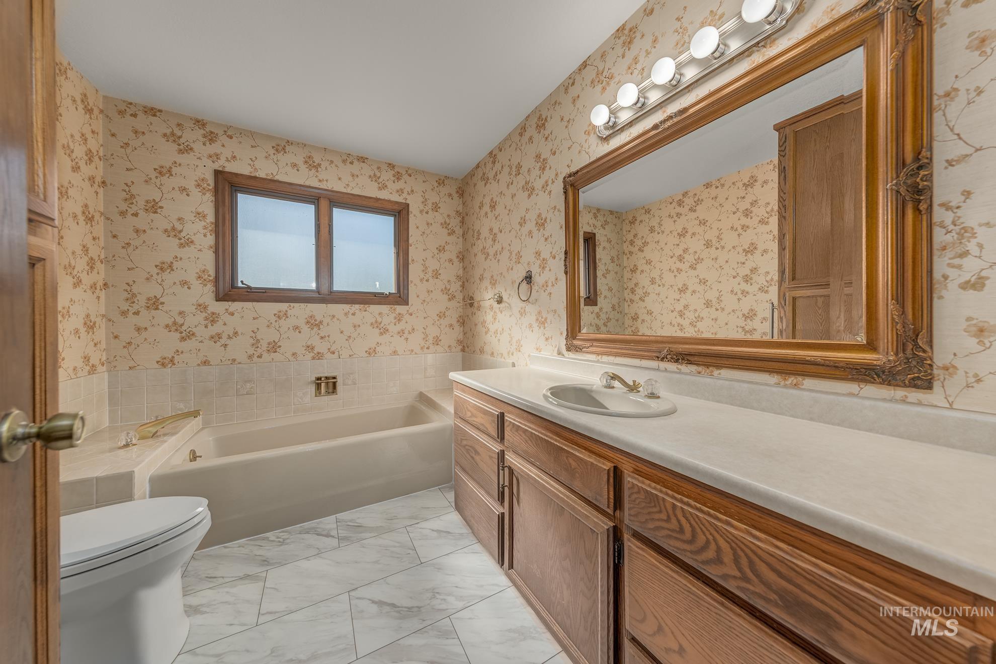 340 Pioneer Road Weiser, ID 83672 - Photo 12 of 44 Bathroom featuring a built-in tub, dual-pane window, wood-finish vanity with an integrated sink, and an ornate framed mirror