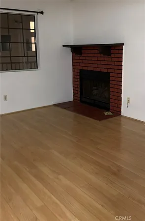 a view of an empty room with wooden floor fireplace and a window