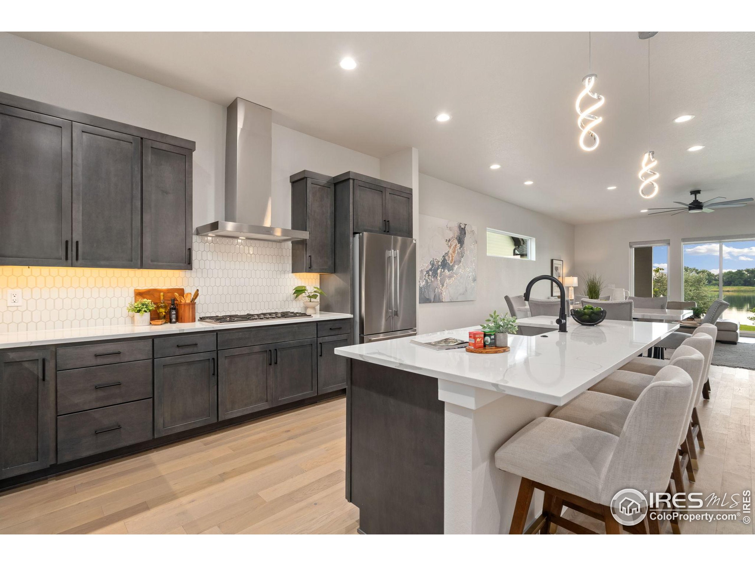 1729 Beachside Drive Windsor, CO 80550 - Photo 7 of 49 a kitchen with stainless steel appliances kitchen island granite countertop a sink dishwasher stove and refrigerator with wooden floor