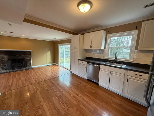 a kitchen with granite countertop a stove a sink and white cabinets with wooden floor