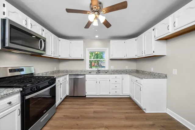a kitchen with stainless steel appliances granite countertop a stove a sink dishwasher and a microwave oven on the wooden floor