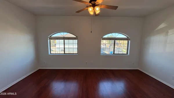 an empty room with wooden floor chandelier fan and windows