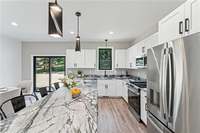 a kitchen with stainless steel appliances a stove a sink dishwasher a refrigerator white cabinets and wooden floor