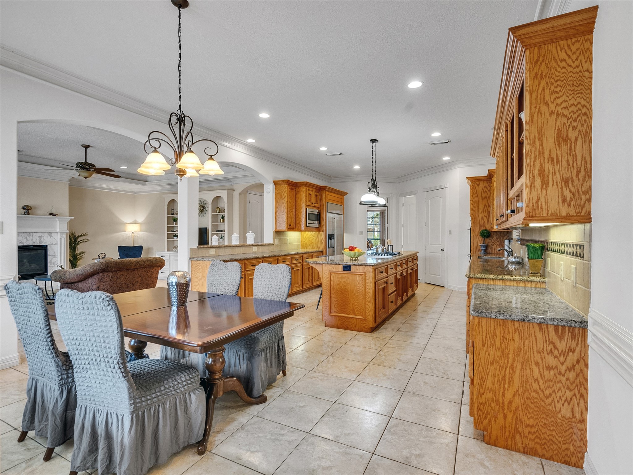 6914 Sandwedge Point Court Spring, TX 77389 - Photo 21 of 50 This spacious kitchen features warm wood cabinetry, a large island with granite countertops, and tile flooring. It's open to a cozy living area with a fireplace, ideal for entertaining.