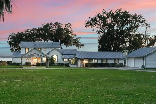 a view of a house next to a big yard and large trees