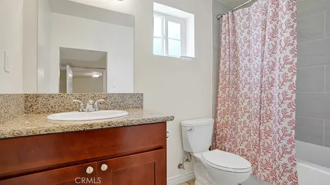 a bathroom with a granite countertop sink a toilet a mirror and shower curtain