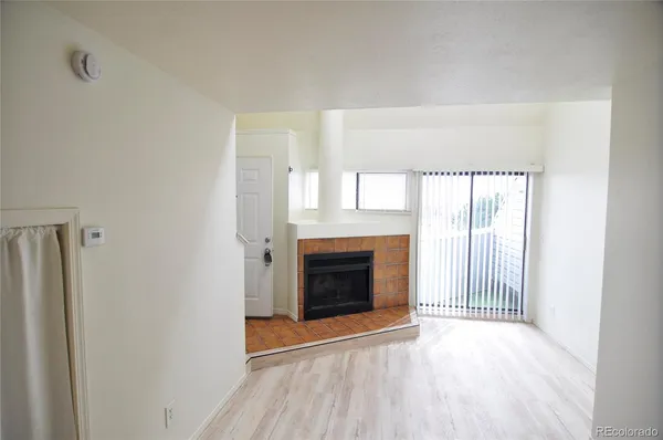 a view of an empty room with wooden floor fireplace and a window
