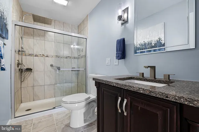 a bathroom with a granite countertop sink a toilet a mirror and shower