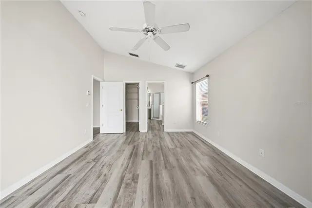 a view of an empty room with wooden floor and a ceiling fan