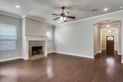 an empty room with wooden floor a ceiling fan a fireplace and windows