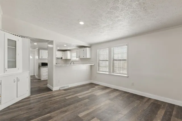 a view of a kitchen and an empty room with wooden floor and a kitchen