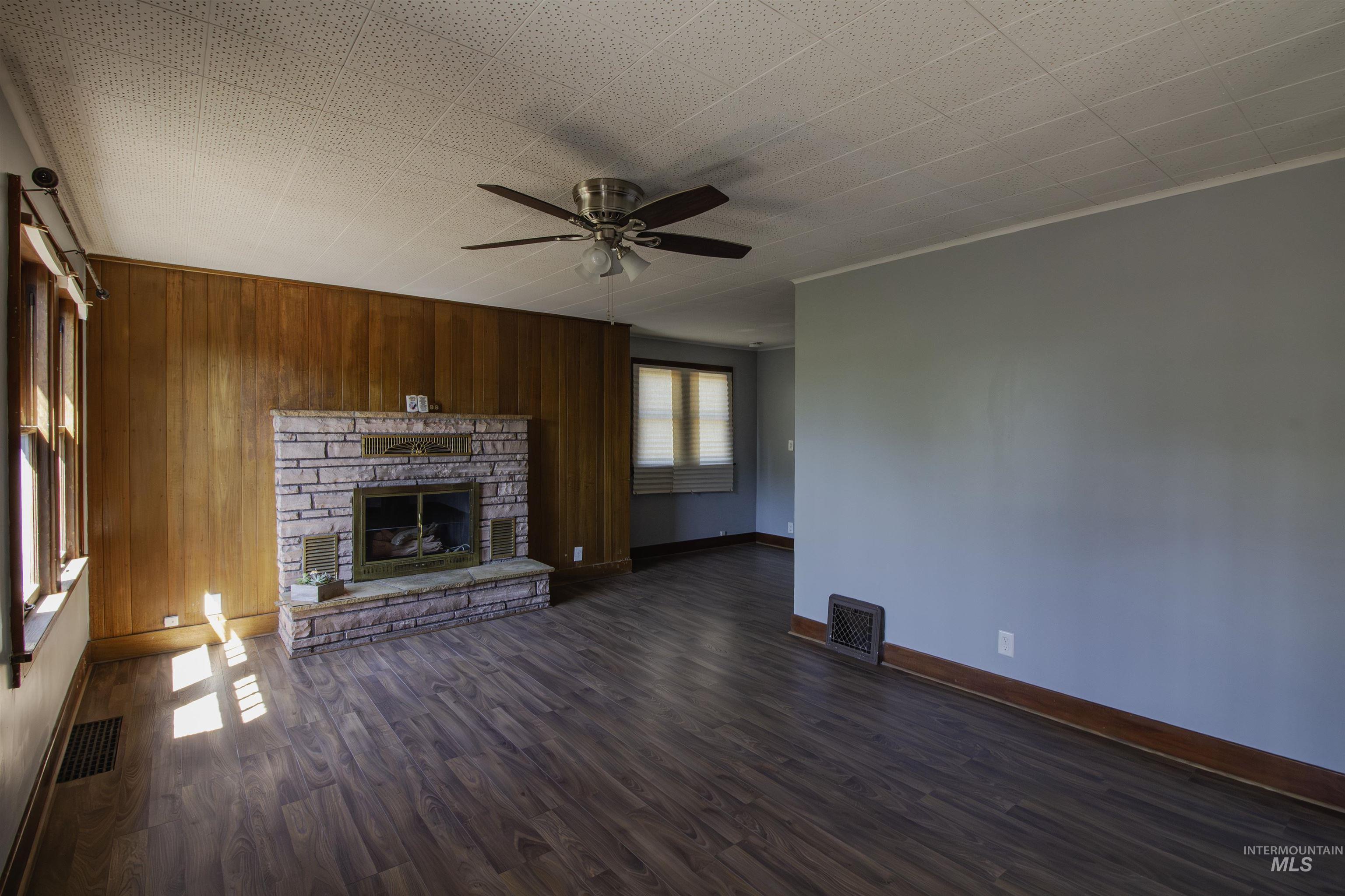 161 Southeast 5th Avenue Ontario, OR 97914 - Photo 37 of 41 Unfurnished living room with wood walls, dark wood-style floors, a fireplace, ceiling fan, and crown molding