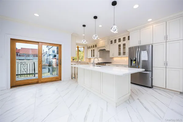 a large white kitchen with stainless steel appliances kitchen island granite countertop a refrigerator a stove a sink a dining table and chairs with wooden floor