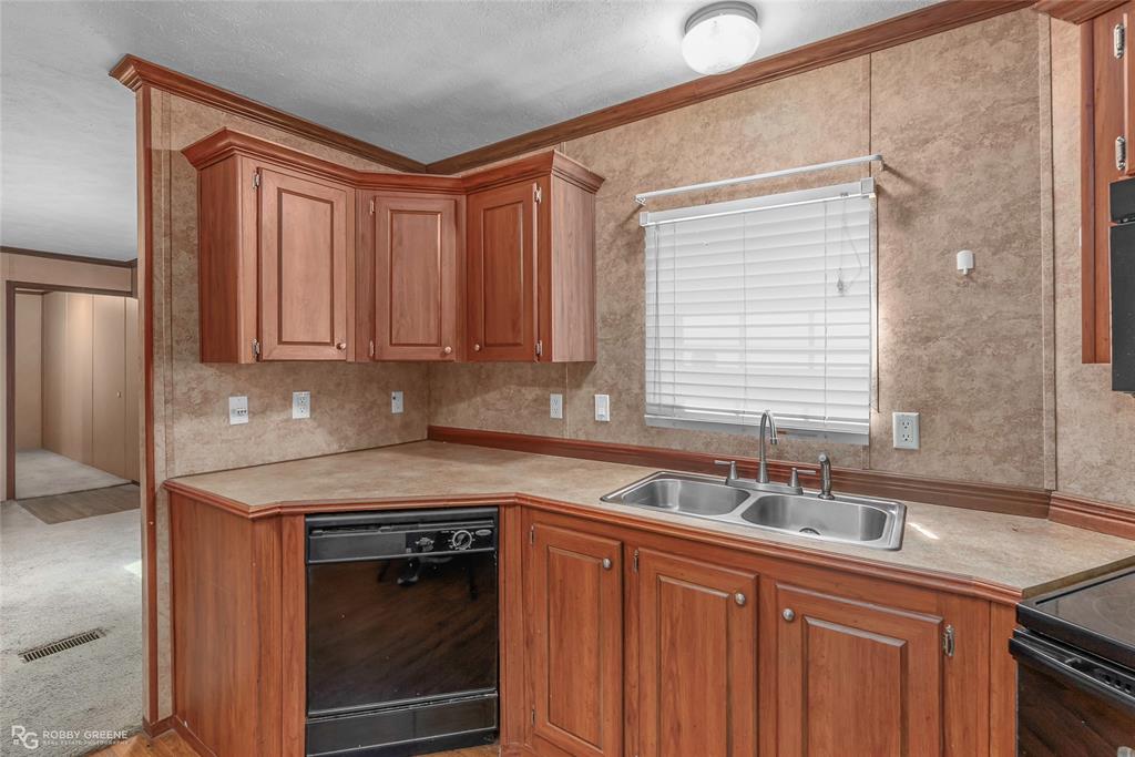 209 Addison Road Mansfield, LA 71052 - Photo 11 of 25 Kitchen featuring light countertops, black appliances, brown cabinetry, ornamental molding, and a textured ceiling