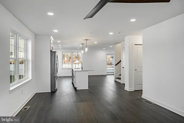 a view of an empty room and a kitchen with wooden floor and a window