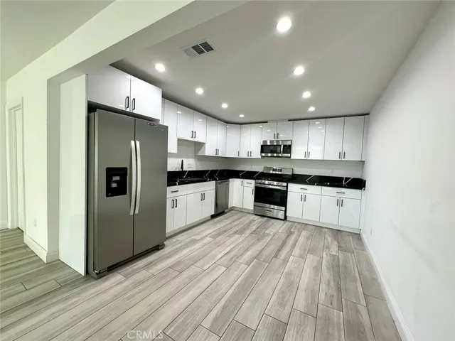 a kitchen with stainless steel appliances granite countertop a refrigerator oven a sink dishwasher and white cabinets with wooden floor