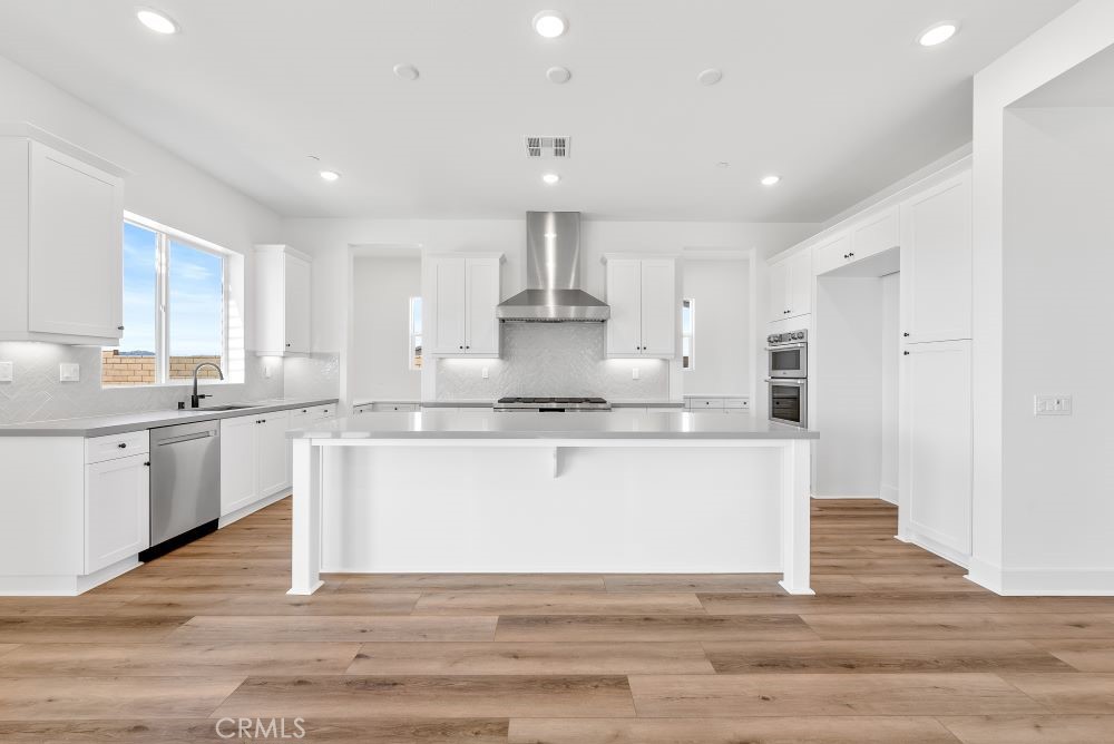 29818 Old Ranch Circle Castaic, CA 91384 - Photo 8 of 41 a large white kitchen with kitchen island a sink dishwasher a stove and white cabinets with wooden floor