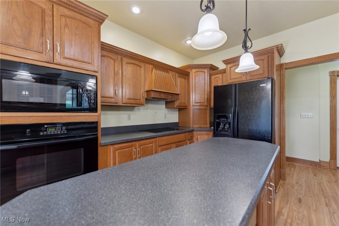 45230 Cemetery Road Wellington, OH 44090 - Photo 10 of 50 Kitchen featuring black appliances, custom range hood, dark countertops, light wood-style flooring, and decorative light fixtures