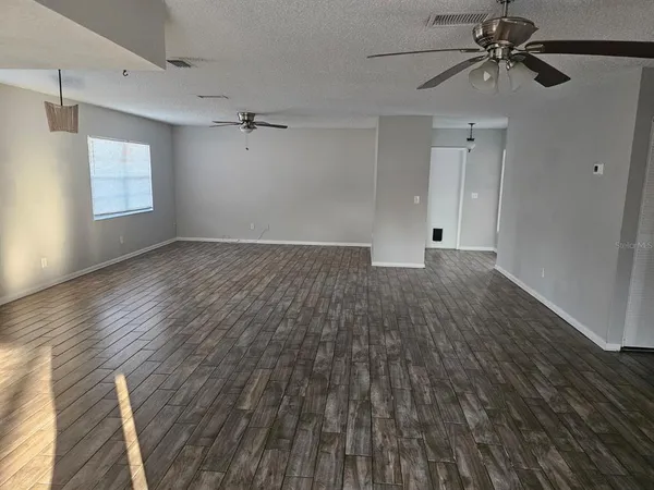 an empty room with wooden floor ceiling fan and windows