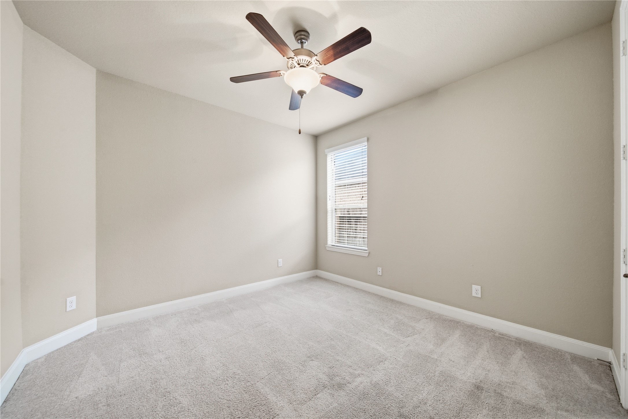5303 Mesquite Willow Lane Rosharon, TX 77583 - Photo 22 of 32 This secondary bedroom located downstairs features soft carpeting, neutral walls, a modern ceiling fan, and a window allowing natural light, creating a cozy and inviting space.