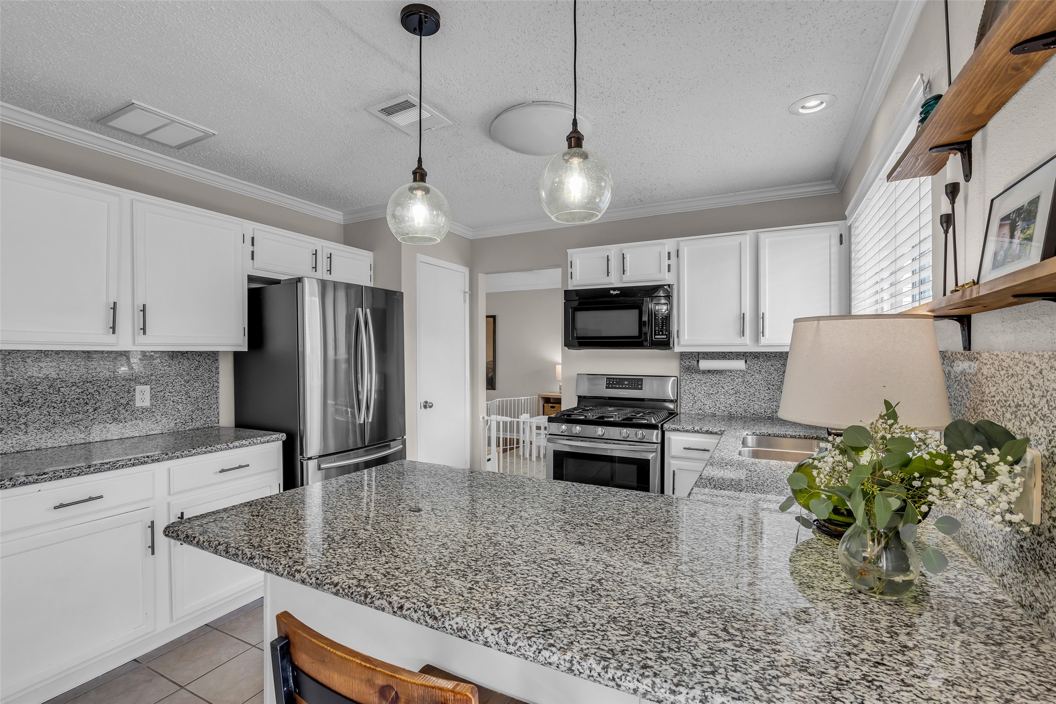 9415 Towerstone Drive Spring, TX 77379 - Photo 18 of 41 This photo showcases a bright, open kitchen with granite countertops, modern appliances, and a view into a cozy living room. Large windows and glass doors provide ample natural light, with a glimpse of a backyard play area outside.