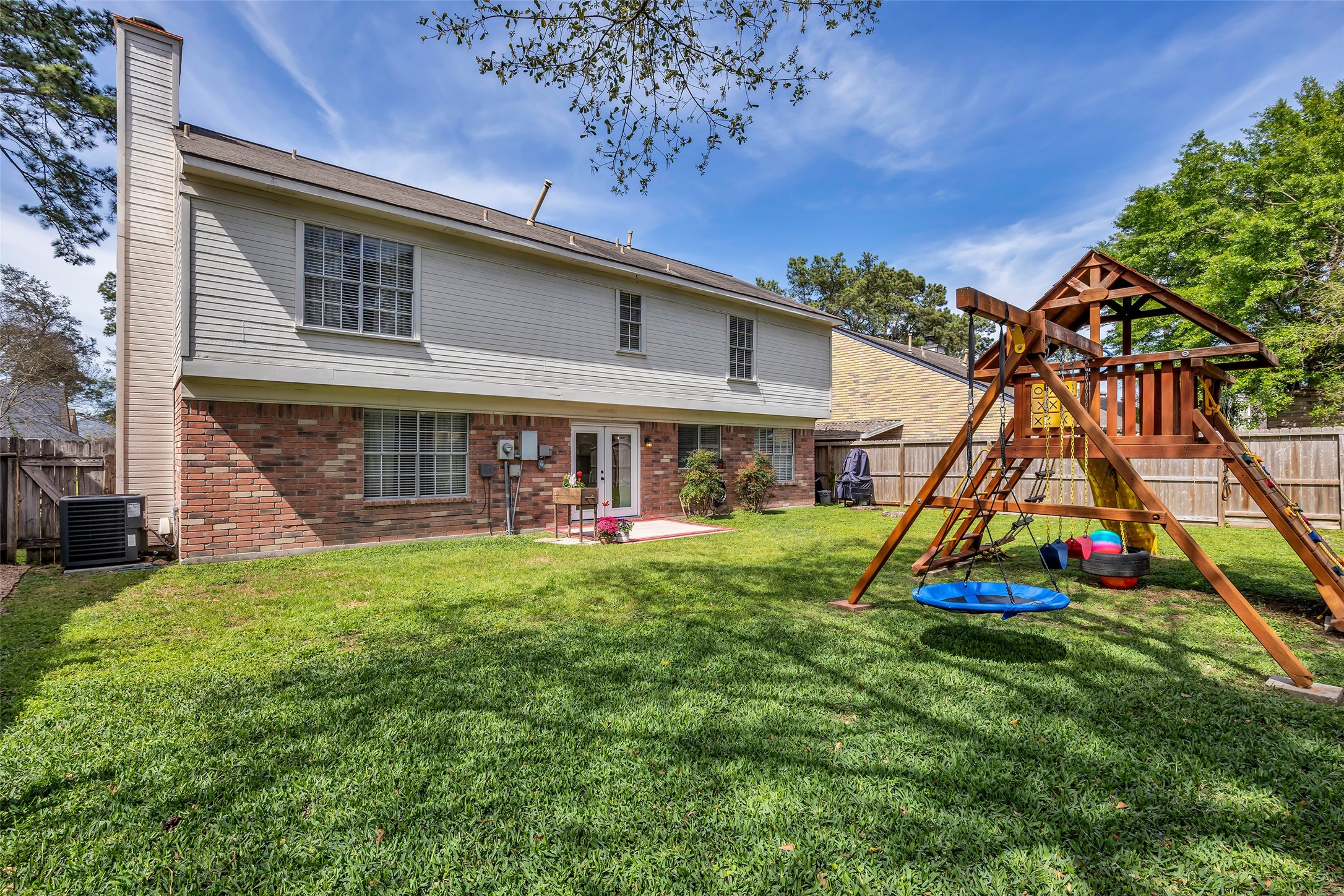 9415 Towerstone Drive Spring, TX 77379 - Photo 2 of 41 Spacious backyard with a lush lawn, featuring a wooden playset and slide. There's a cozy patio area with a small outdoor rug, surrounded by a wooden fence for privacy. Ideal for families and outdoor activities.