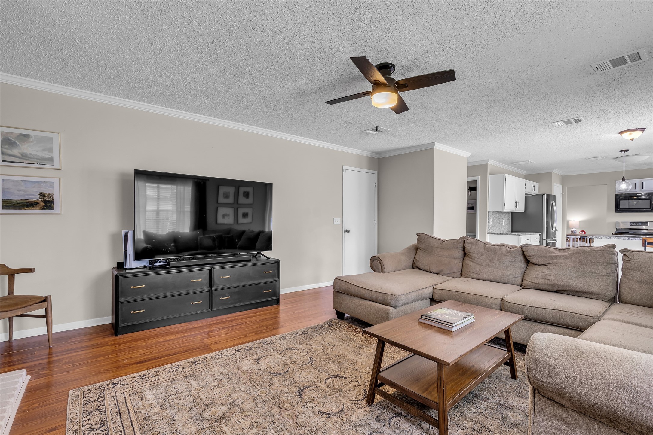 9415 Towerstone Drive Spring, TX 77379 - Photo 23 of 41 This inviting living room features a cozy sectional sofa, a classic white brick fireplace, and a large TV. The space is accented with a ceiling fan, hardwood floors, and tasteful decor, creating a warm and comfortable atmosphere.