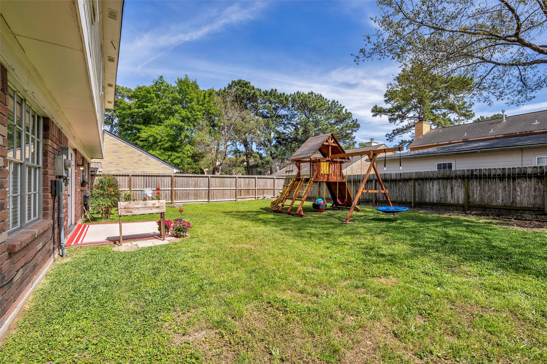 9415 Towerstone Drive Spring, TX 77379 - Photo 34 of 41 The photo showcases a spacious backyard with a well-maintained lawn, a children's playset featuring a slide and swings, and a brick exterior of a two-story home. There's a patio area with plants and a grill, providing a great space for family activities and outdoor entertaining.