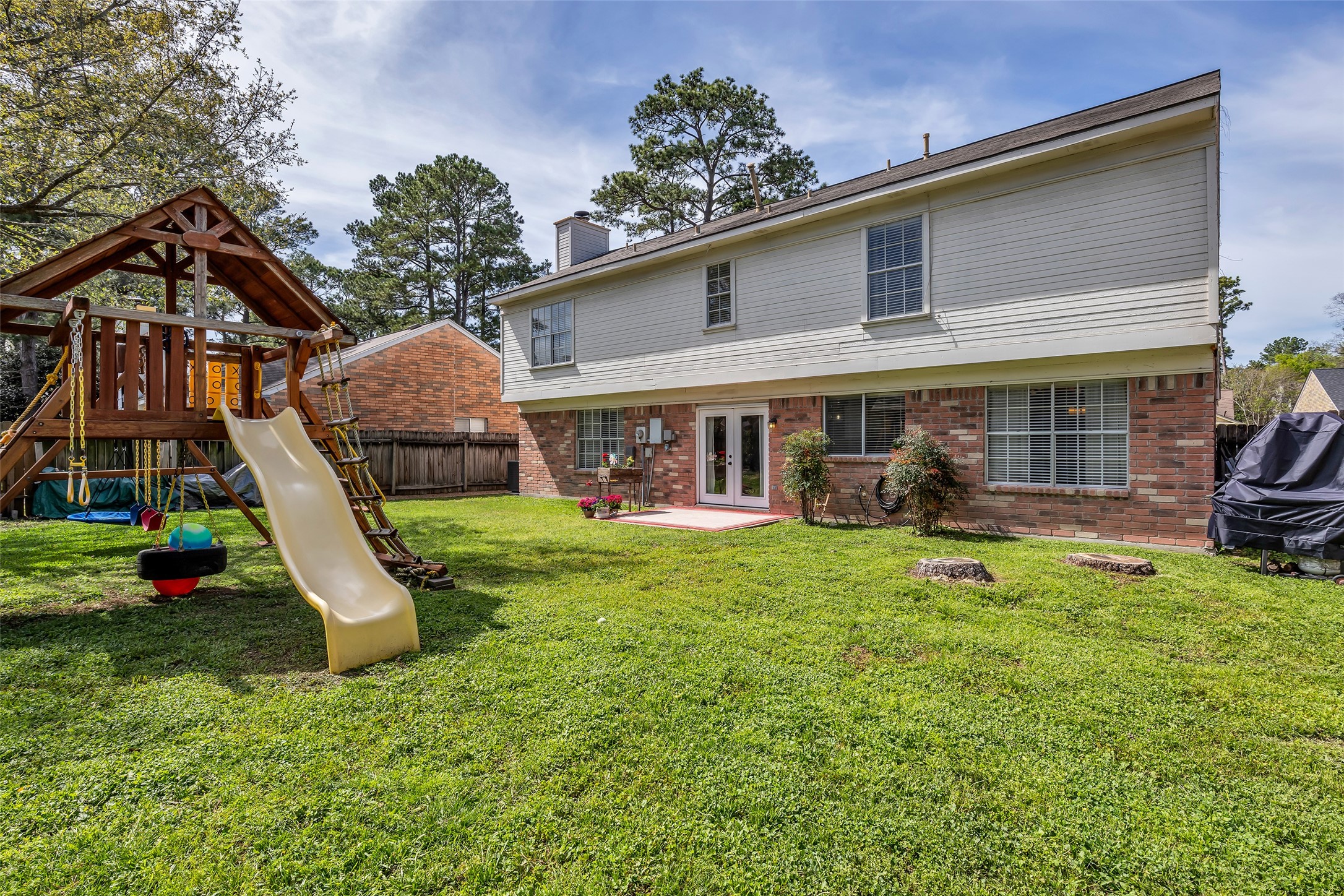 9415 Towerstone Drive Spring, TX 77379 - Photo 35 of 41 Spacious backyard with a playset, mature trees, and a well-maintained lawn, perfect for families. A wooden fence provides privacy, and there are a few colorful flowers near the patio area.