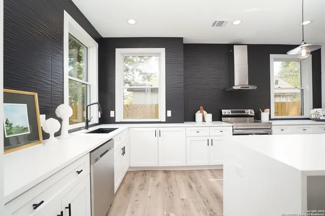 a large white kitchen with a window wooden floor and stainless steel appliances