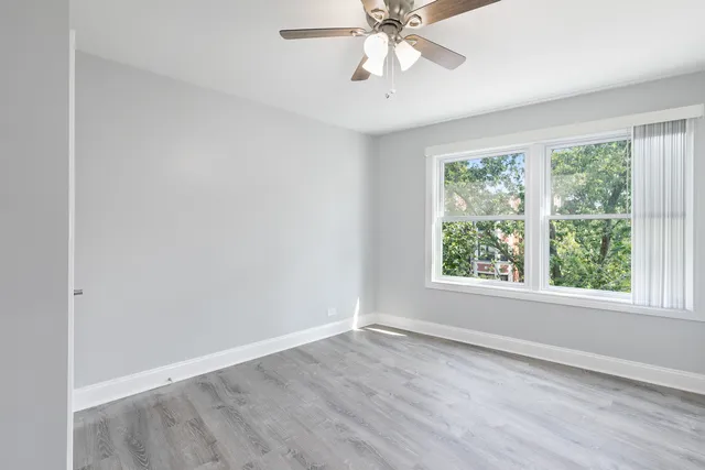 an empty room with wooden floor fan and windows