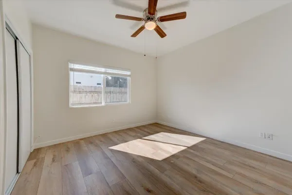 an empty room with wooden floor chandelier fan and windows