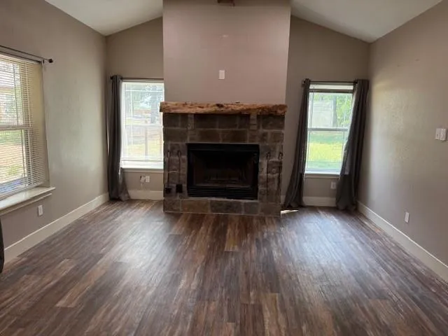 an empty room with wooden floor fireplace and windows