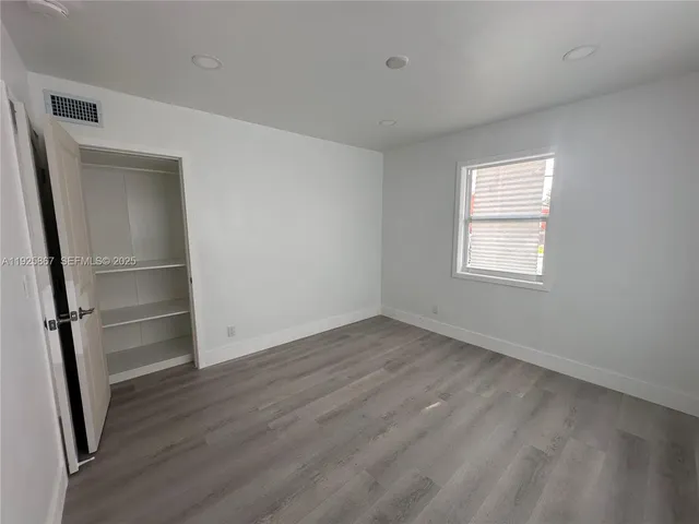 a view of an empty room with wooden floor fridge and a window