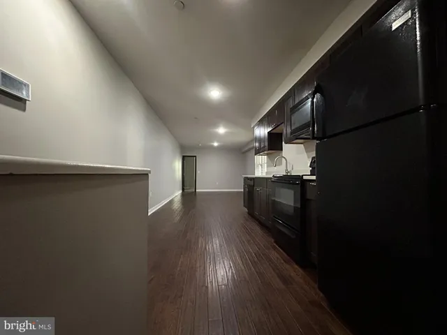 a view of a refrigerator in kitchen and an empty room with wooden floor