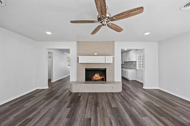 a view of a livingroom with a fireplace a ceiling fan and wooden floor