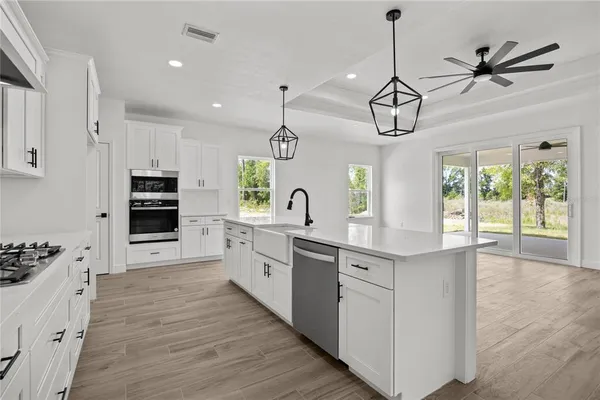 a kitchen with stainless steel appliances kitchen island granite countertop a stove a sink and white cabinets with wooden floor