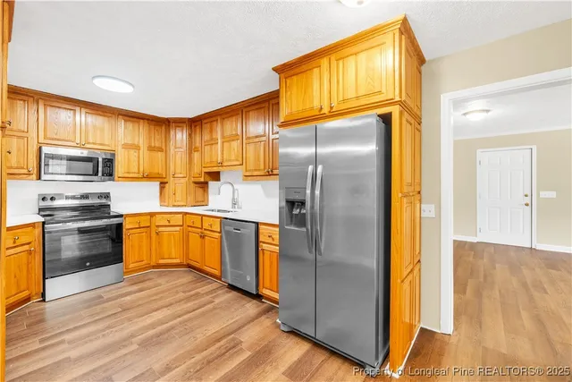 a kitchen with stainless steel appliances granite countertop a refrigerator a sink dishwasher a oven with wooden cabinets and wooden floor