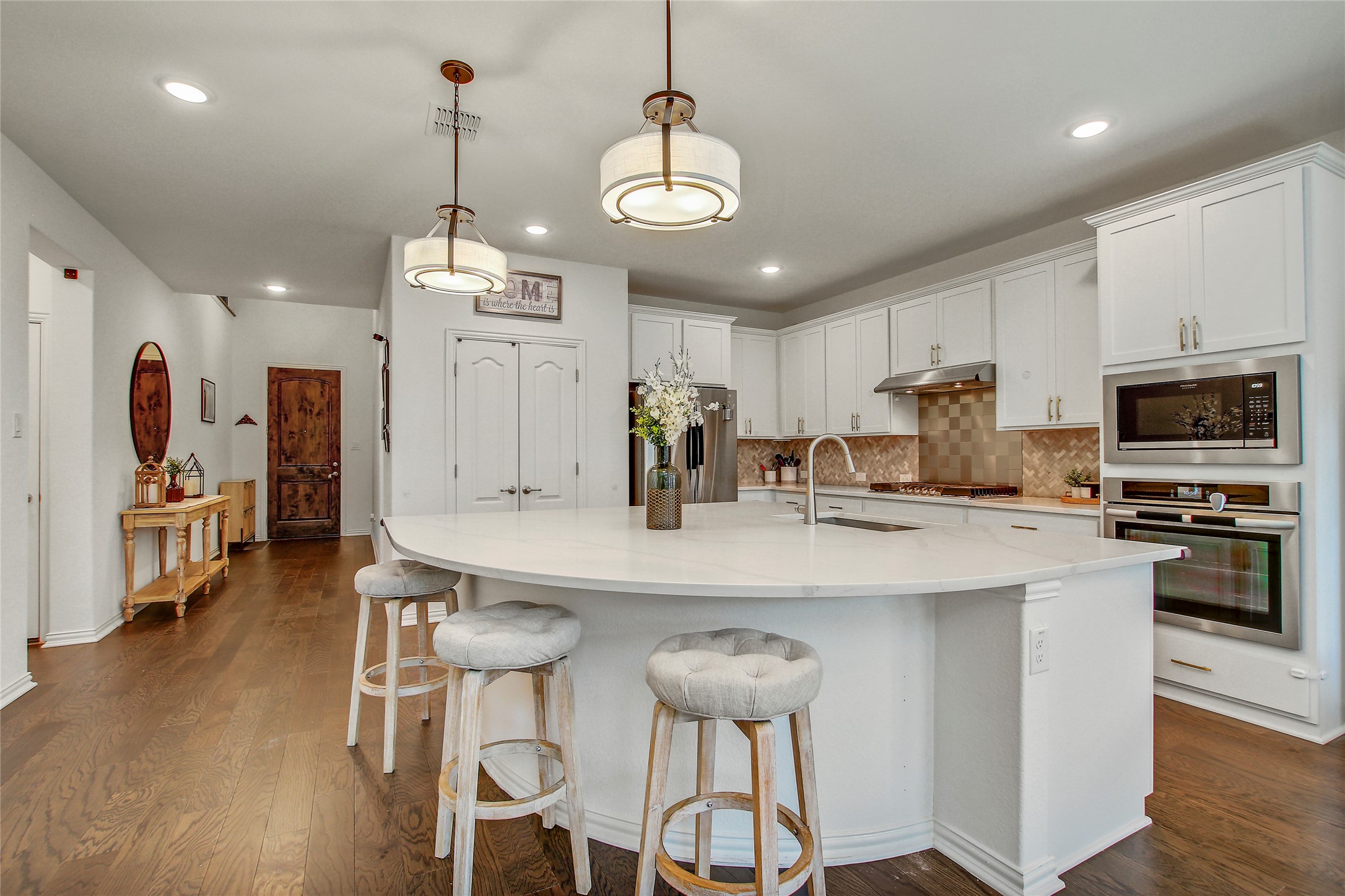 104 Millbend Road Georgetown, TX 78633 - Photo 9 of 40 A pristine culinary space boasts a large island, premium appliances, and rich hardwood flooring, extending into the entryway.