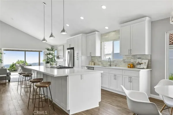 a kitchen with stainless steel appliances kitchen island granite countertop a dining table chairs and white cabinets