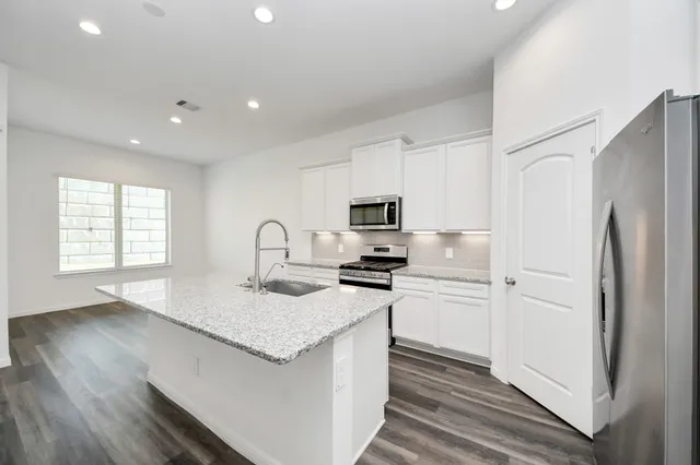 a kitchen with stainless steel appliances granite countertop a refrigerator a stove a sink and white cabinets with wooden floor